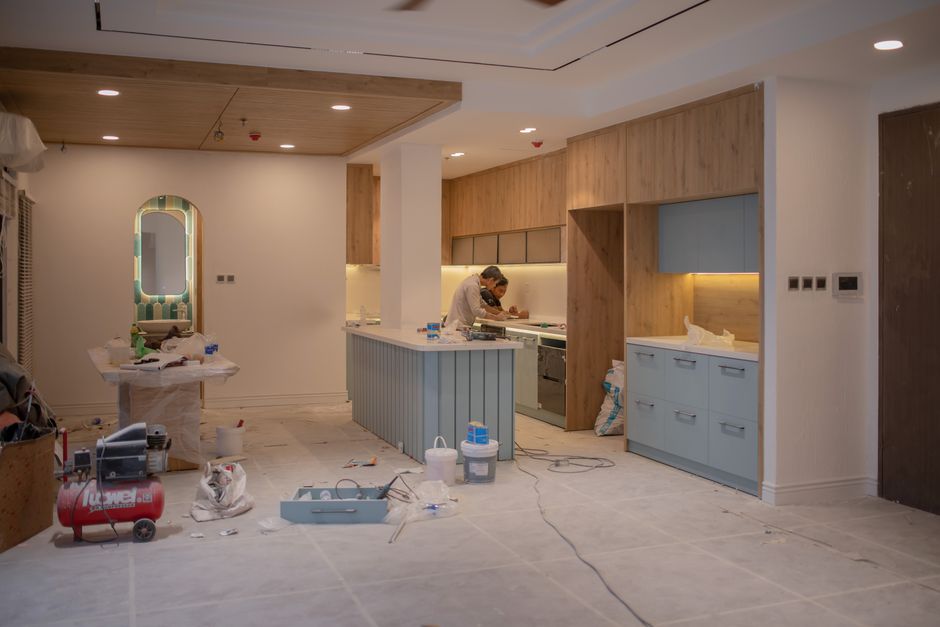 A spacious, partially renovated kitchen area with a white ceiling and walls, featuring large windows allowing natural light to flood the room. The floor appears to be bare, possibly awaiting finishing